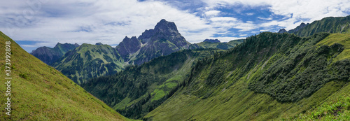 Panorama grüne Berghänge in den Alpen mit faszinierenden Wolken am blauen Himmel