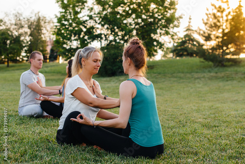 A group of people perform paired yoga exercises in a Park during sunset. Healthy lifestyle, meditation and Wellness © Andrii