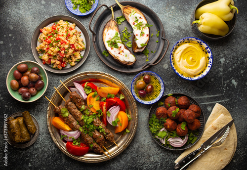 Middle eastern or Mediterranean dinner with grilled kebab, falafel, roasted and fresh vegetables, assorted Arabic meze and appetizers served on rustic background table. Dinner table overhead 