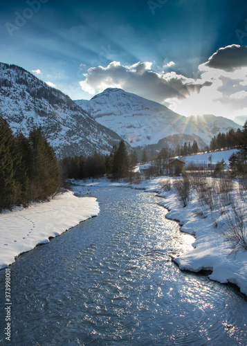 Winterliche Flusslandschaft mit Schnee und Bergen bei Sonnenuntergang