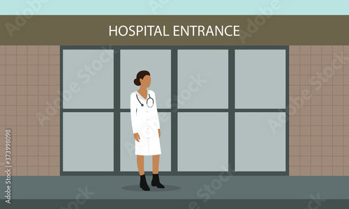 Female doctor in white coat with a stethoscope is standing in front of the hospital entrance