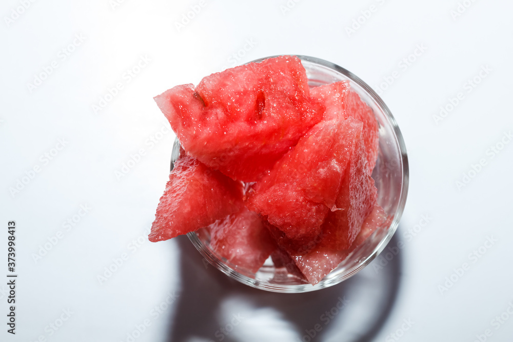 ripe watermelon cut into pieces in a glass for whiskey on a white background. ripe watermelon cut into pieces in a glass for whiskey on a white background.