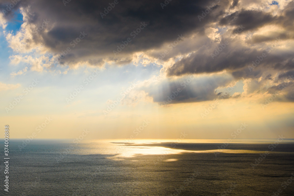 Large dark clouds over the sea. The sun's rays shine through the clouds and are reflected on the sea.