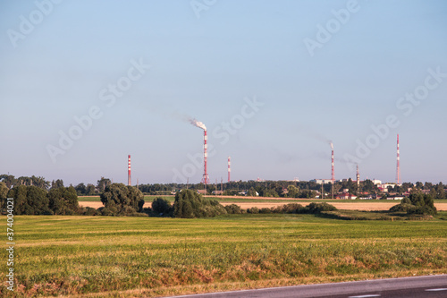 Pipes of a chemical plant against the background of the sky, fields and trees.