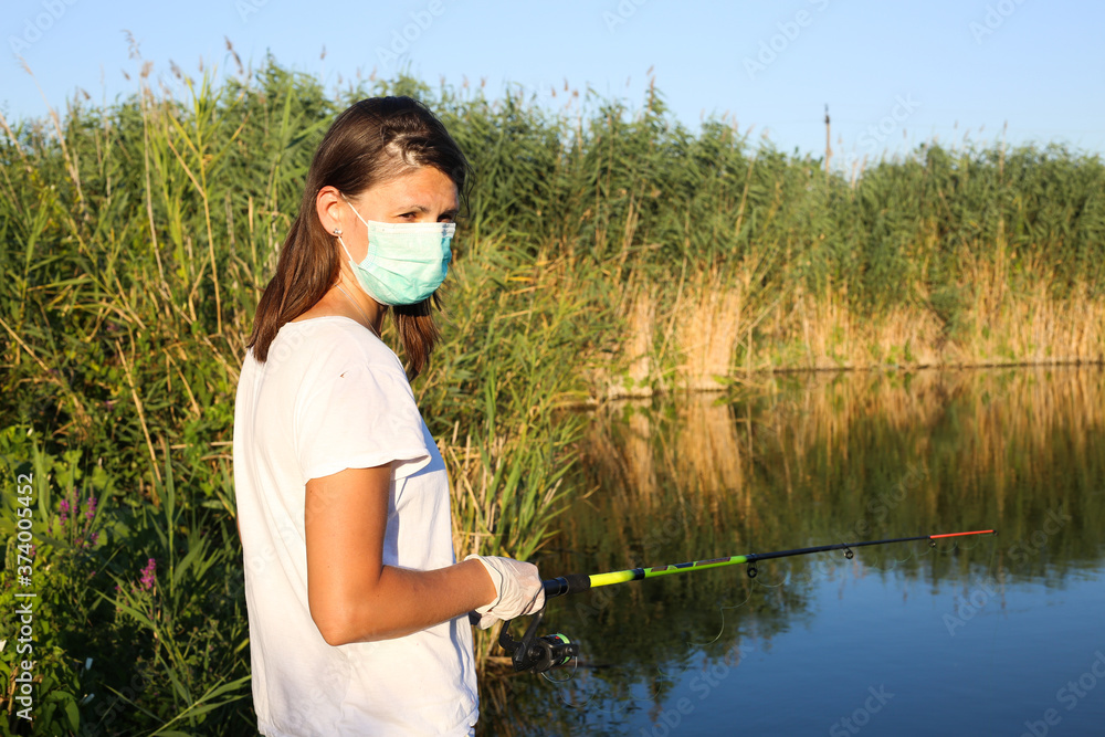 Young woman fishing at the river wearing medical face mask
