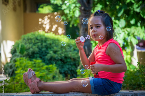 Little girl dressed in casual clothes is blowing bubbles in the garden