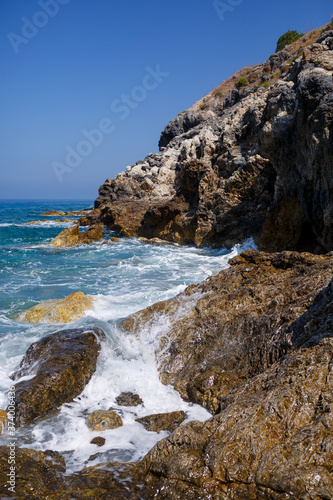 Wonderful views of the blue Mediterranean Sea. Sunny rocks, waves with foam and splashing water. The wave crashes into the rocks on the shore © Дмитрий Ткачук