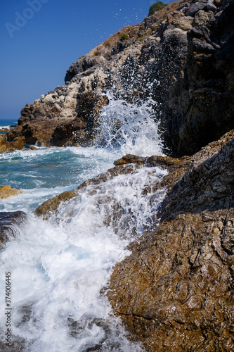 Wonderful views of the blue Mediterranean Sea. Sunny rocks, waves with foam and splashing water. The wave crashes into the rocks on the shore