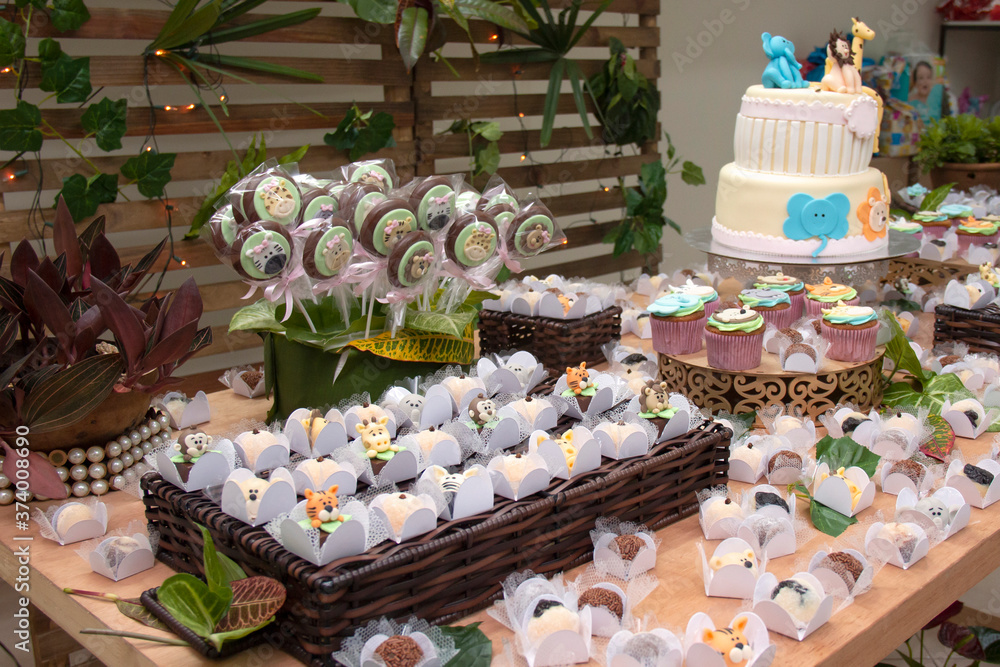 Children's table decoration with birthday cake, candies, cupcake, chocolates and brigadeiro on the rustic wooden table.
