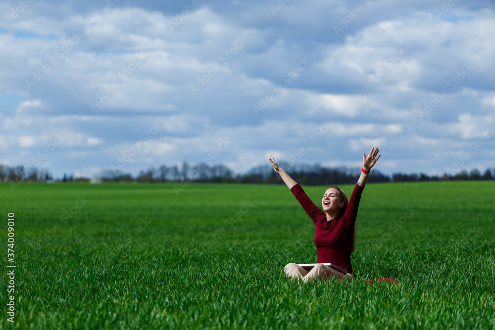 Young successful woman is sitting on green grass with a laptop in her hands. Rest after a good working day. Work on the nature. Student girl working in a secluded place. Workplace in nature Young successful woman is sitting on green grass with a laptop in her hands. Rest after a good working day. Work on the nature. Student girl working in a secluded place. Workplace in nature