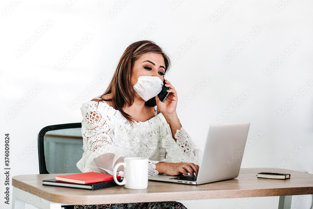 Mexican middle aged woman talking by phone using face mask at office or workplace in Mexico pandemic Mexican middle aged woman talking by phone using face mask at office or workplace in Mexico pandemic