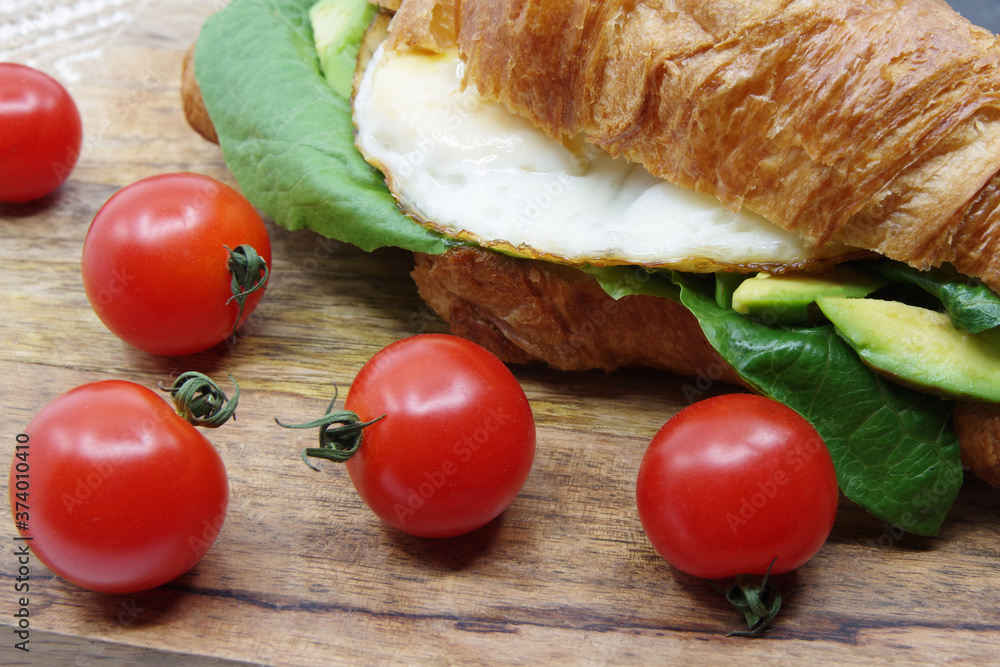 Croissant stuffed fried egg and avocado on a wooden tray Croissant stuffed fried egg and avocado on a wooden tray
