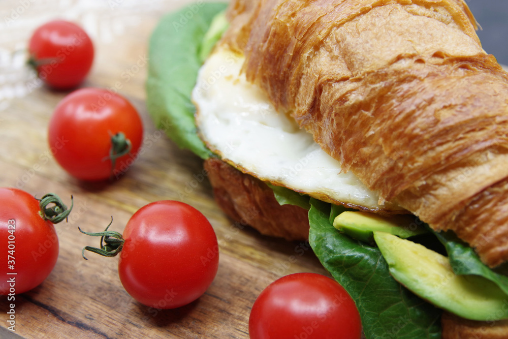 Croissant stuffed fried egg and avocado on a wooden tray Croissant stuffed fried egg and avocado on a wooden tray