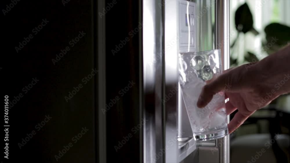 Drinking water from fridge filling up glass of water with ice for