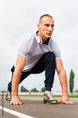 Low angle view on adult caucasian man stretching on the running track - Blonde male athlete preparing for training in summer day - real people healthy lifestyle concept