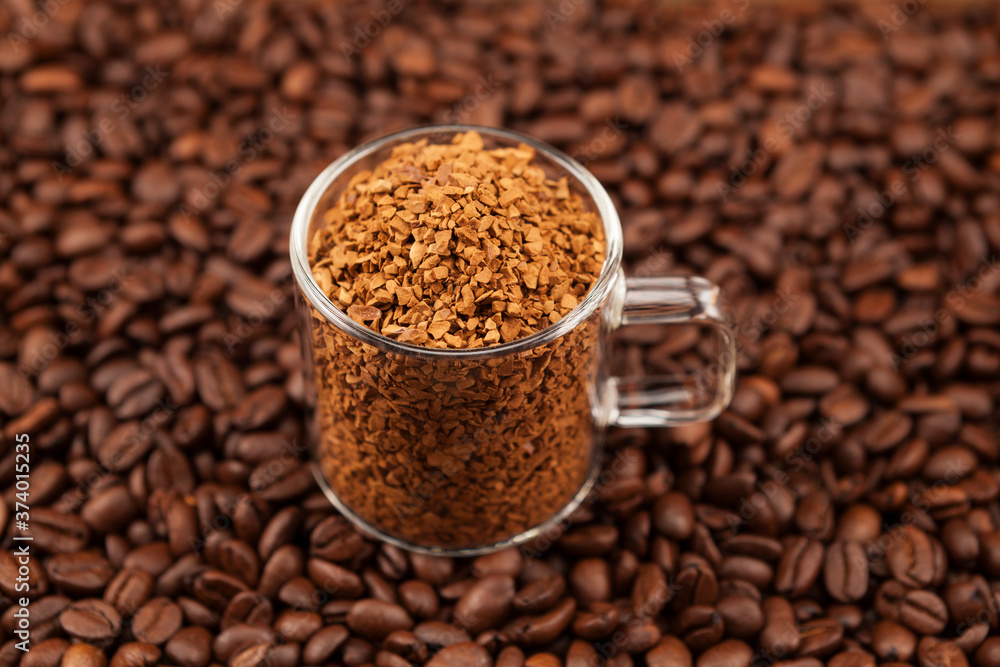 Instant, freeze-dried or granulated coffee in a transparent cup on the background of roasted coffee beans. Used to make a cold Dalgon coffee drink. Selective focus Instant, freeze-dried or granulated coffee in a transparent cup on the background of roasted coffee beans. Used to make a cold Dalgon coffee drink. Selective focus