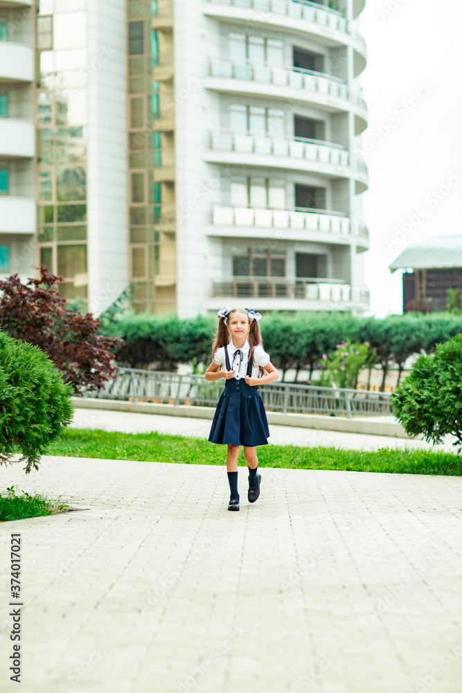 a beautiful girl, in a blue school uniform, with a school backpack, near the school building. Return to school, September 1