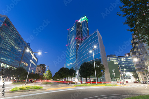 Milan, Italy - August 25, 2020: long exposition shot featuring a street view of Milan at dusk. Light trails are visible in twilight in front of Regione Lombardia headquarters skyscraper.