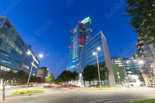Milan, Italy - August 25, 2020: long exposition shot featuring a street view of Milan at dusk. Light trails are visible in twilight in front of Regione Lombardia headquarters skyscraper.