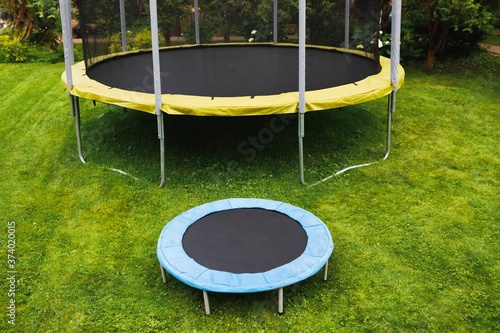 small trampoline near big one with round mat, size comparison, green lawn background photo