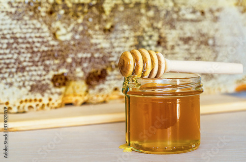 glass jar of honey with wooden dipper on background of frame with honeycombs. copy space, place for text