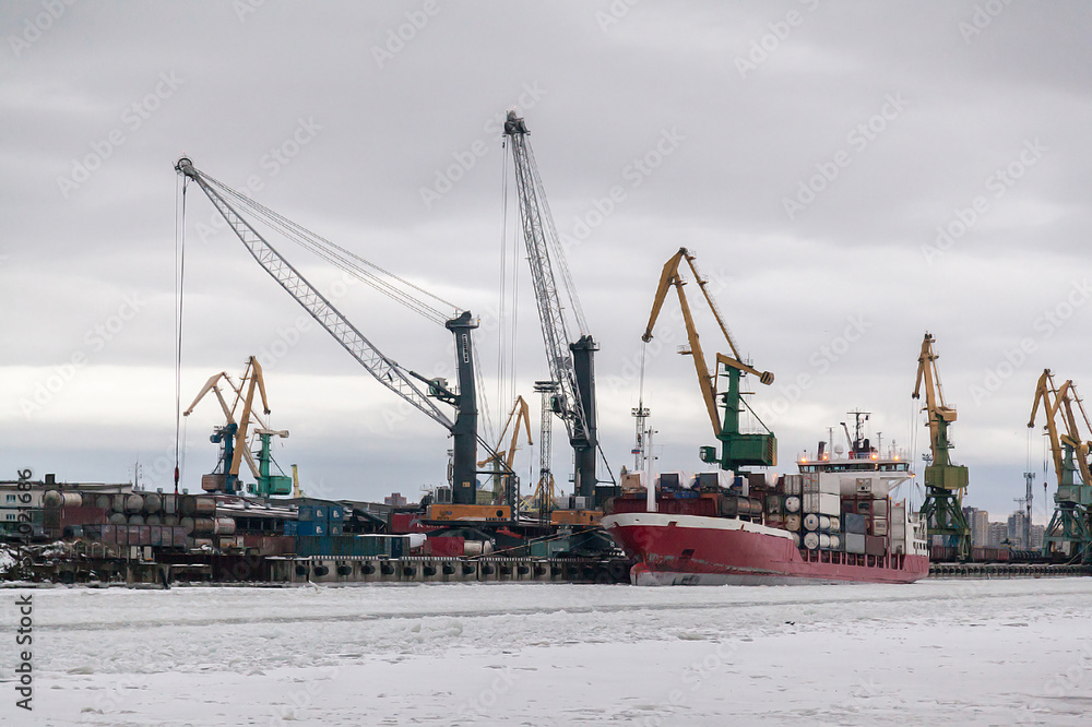 Red cargo ship at the winter stop in the industrial port frozen in the ice Red cargo ship at the winter stop in the industrial port frozen in the ice