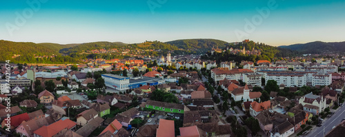 Drone aerial evening panorama of Sighisoara, Romania with Citadel and Biserica din Deal rising above the skyline. View towards the beautiful old town.
