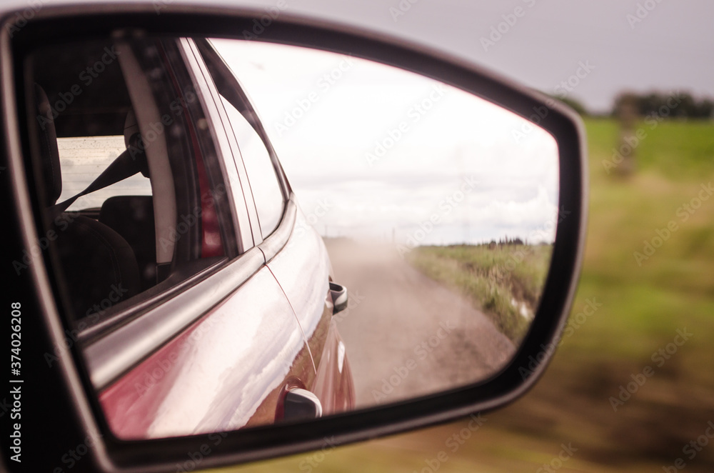  Rearview mirror reflection of a car on a dusty road.