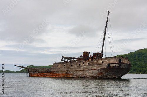 An old wooden Soviet whaling boat, the ship ran aground on the Bay shore, the front background is the sea shore, the background is the horizon with peninsulas, Vityaz Bay. © Evgeniy
