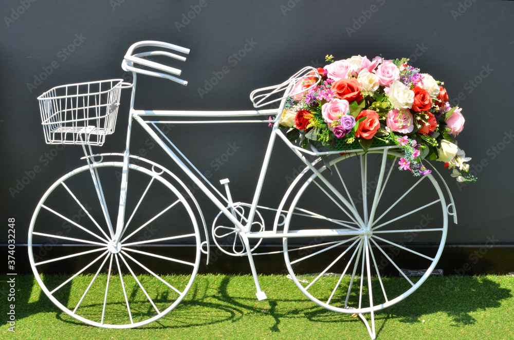 White bicycle with flowers on green grass beside the wall