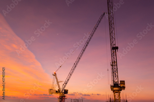 Huge crane and construction plant.Tower Crane in Construction site. Industrial construction cranes and building silhouettes over sun at sunrise.Construction crane and skyscraper at sunset
