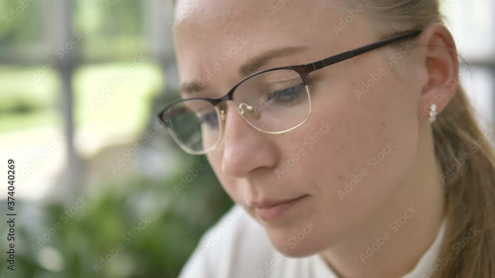 pensive young woman in stylish eyeglasses with blonde ponytail looks at something on green blurred background in cafe extreme closeup pensive young woman in stylish eyeglasses with blonde ponytail looks at something on green blurred background in cafe extreme closeup