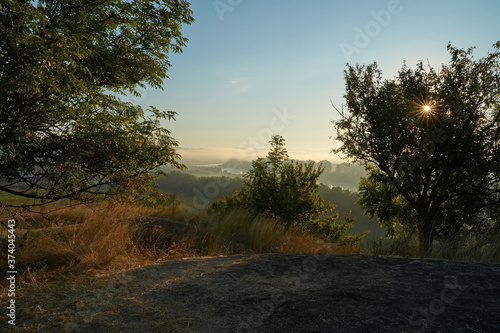 Summer time. Morning dawn over the river in a hazy, thoughtful haze. Beautiful view of the forest and river covered with fog early in the morning.