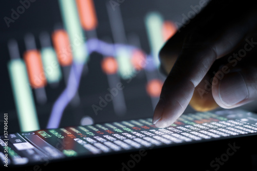 Businessman finger touching screen on smartphone with stock market graph at night.