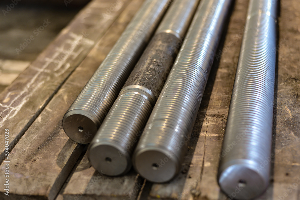 After turning and milling, the threaded studs lie on a wooden rack in the warehouse.