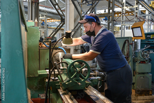 A working turner wearing a protective antiviral mask sets up the machine at the factory.