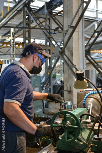 A working turner wearing a protective antiviral mask works on a lathe under quarantine conditions.