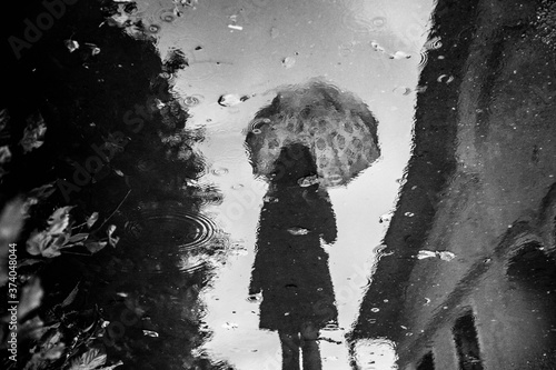 Silhouette of young girll with lace parasol reflected in puddle