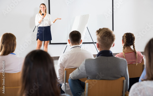 Smiling female coach giving presentation for adult audience in lecture hall .. © JackF