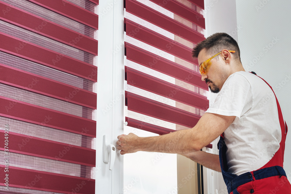 Construction worker man in a uniform installing new window blinds Construction worker man in a uniform installing new window blinds