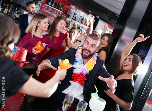 Cheerful guy expressively dancing on corporate party in Hawaiian style in bar