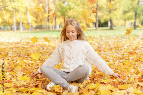 beautiful blonde teen girl sitting on the grass in an autumn Park with maple trees