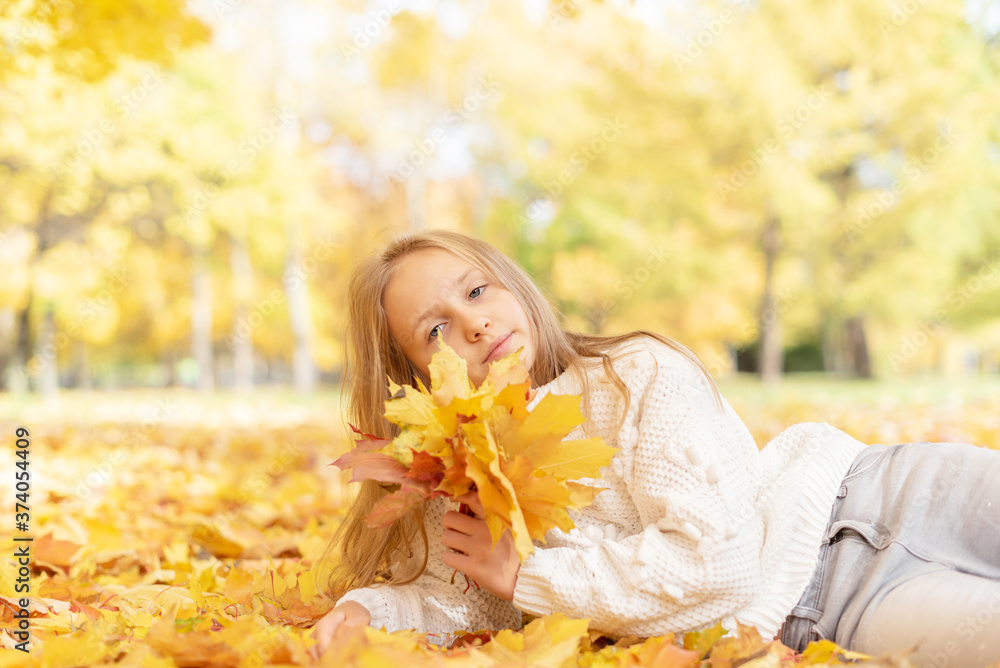 beautiful blonde teen girl sitting on the grass in an autumn Park with maple trees beautiful blonde teen girl sitting on the grass in an autumn Park with maple trees