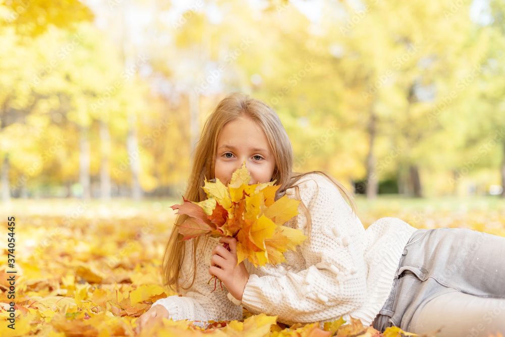 beautiful blonde teen girl sitting on the grass in an autumn Park with maple trees beautiful blonde teen girl sitting on the grass in an autumn Park with maple trees