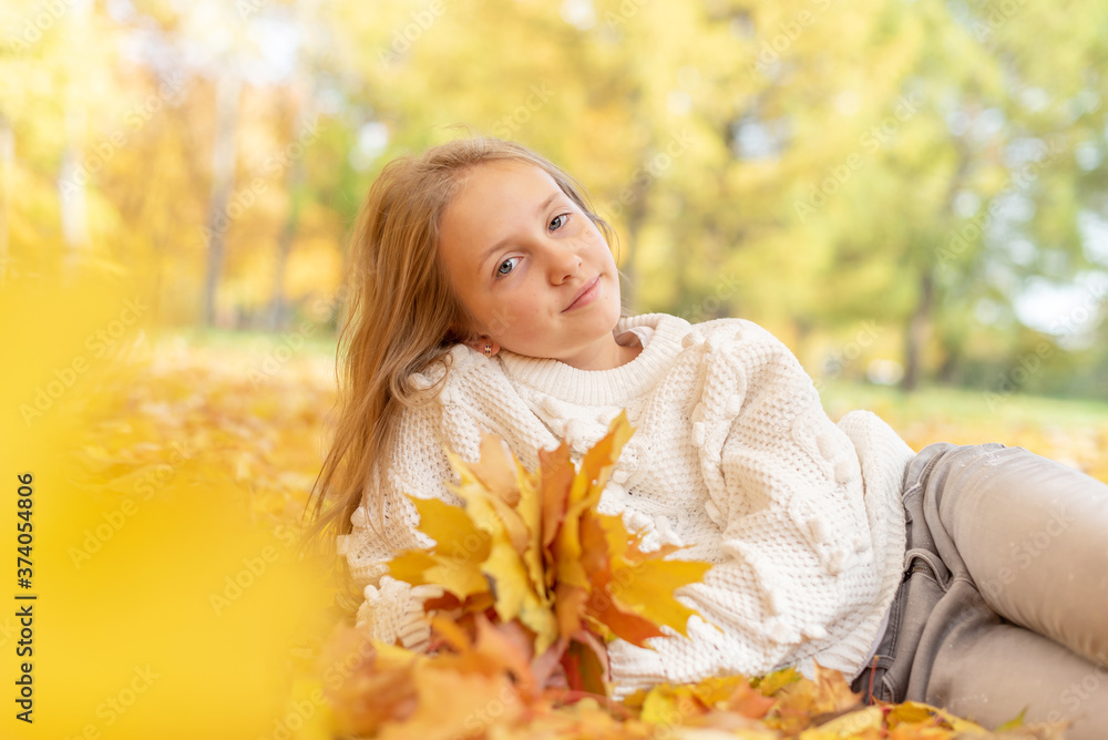 beautiful blonde teen girl sitting on the grass in an autumn Park with maple trees beautiful blonde teen girl sitting on the grass in an autumn Park with maple trees