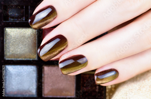 Cat Eye Nail Art. Manicure golden brown on a Gold background. Female fingers with golden brown Nails holding eyeshadow palette.