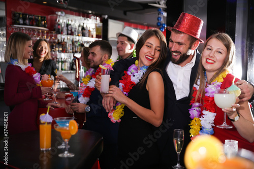 Young man and two women with cocktails having fun on Hawaiian party at nightclub