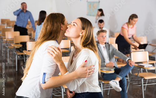 Two girls friendly greeting each other with kiss in auditorium before training course..