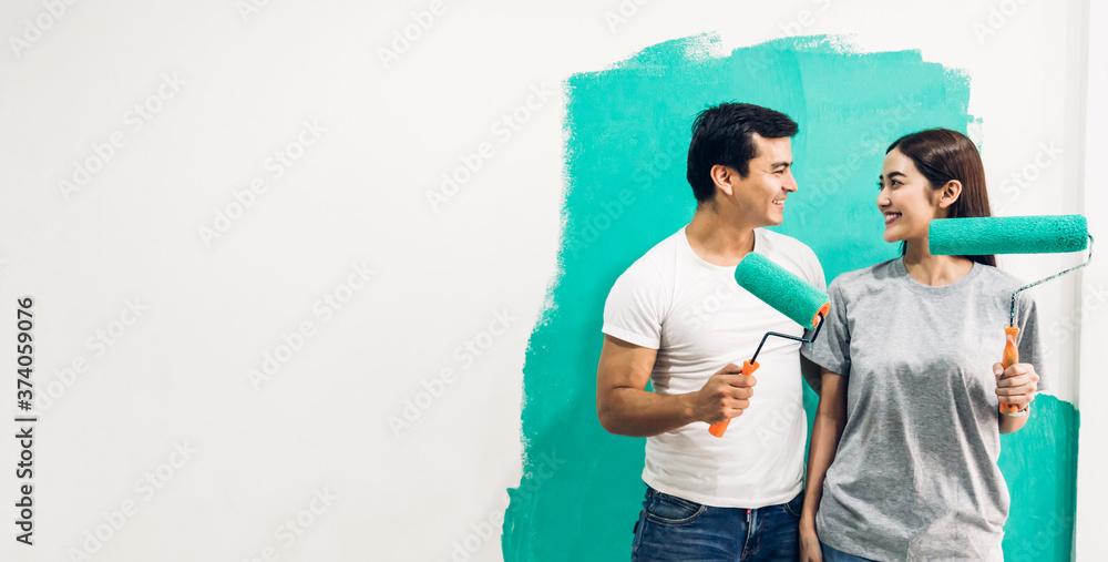 Happy couple using a paint roller and painting walls in their new home