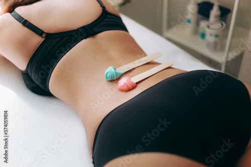 Side view on sticks with hot wax for depilation hair removal procedure on female back. The concept of depilation, epilation, waxing, shugaring.